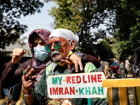 Supporters of former Pakistan Prime Minister Imran Khan, pose with a placard in a shape of a cricket bat, as they gather with others outside Khan's house, in Lahore, Pakistan March 16, 2023.  