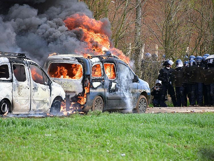 French gendarmes' stand next to gendarmes' cars burning on the sideline of a demonstration called by the collective "Bassines non merci", the environmental movement "Les Soulevements de la Terre" and the French trade union 'Confederation paysanne' to protest against the construction of a new water reserve for agricultural irrigation, in Sainte-Soline, central-western France, on March 25, 2023. 