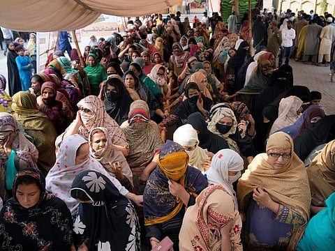 Women wait for their turn to get a free sack of wheat flour at a distribution point, in Lahore, on March 30, 2023. 