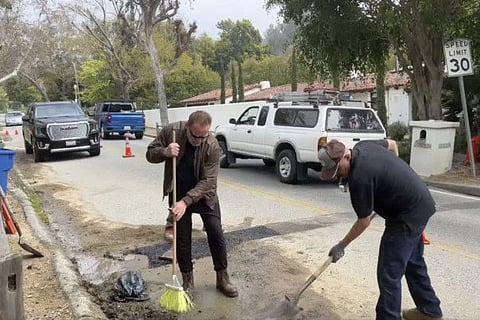 This video still image provided by The Office of Arnold Schwarzenegger, shows former California Governor Arnold Schwarzenegger, left, repairing a pot hole on a street in his Los Angeles neighborhood on Tuesday, April 11, 2023.