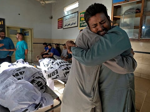 People mourn next to the bodies of fire fighters at a morgue in Karachi, on April 13, 2023.  