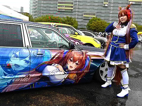 A woman dressed up as anime character Daiwa Scarlet posing next to a car owned by Yosuke Takahata.