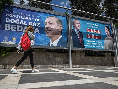 A woman walks past billboards, one reading "1 year free natural gas in residences for the kitchen and hot water" with the portrait of Turkish President Recep Tayyip Erdogan (left) and another with the portrait of Republican People's Party (CHP) leader and presidential candidate, Kemal Kilicdaroglu (right) reading "My promise to you" in Sanliurfa, south-eastern Turkey on April 28, 2023.  