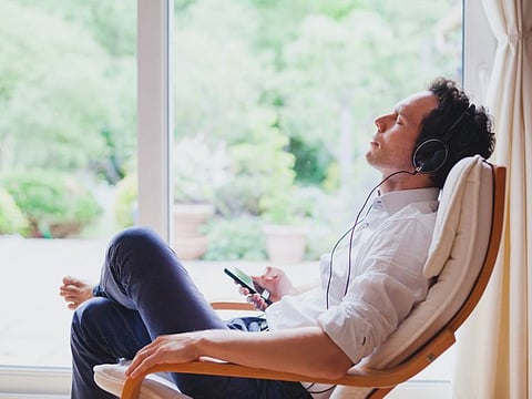 listening relaxing music at home, relaxed man in headphones sitting in deck chair in modern bright interior