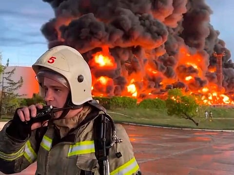 In this handout photo made from video released by the Governor of Sevastopol Mikhail Razvozhaev telegram channel on Saturday, April 29, 2023, a firefighter speaks on the walkie talkie as smoke and flame rise from a burning fuel tank in Sevastopol, Crimea.  