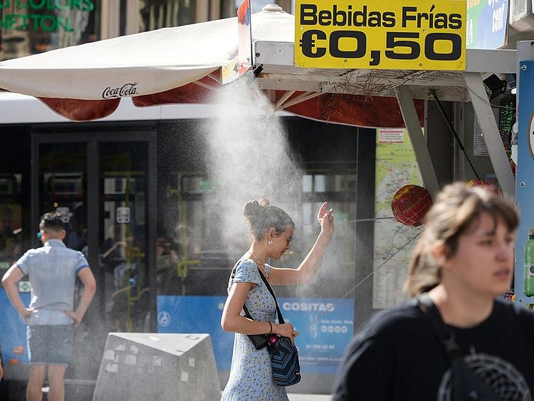 A customer stands under a cooling mist spray at a street kiosk during high temperatures in central Madrid, Spain, on Thursday, April 27, 2023.  