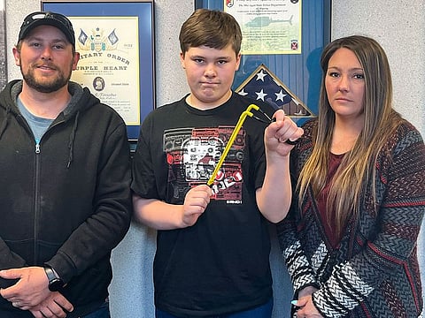 Andrew Burns, left, Owen Burns, center, and Margaret Burns pose with a slingshot Owen used to thwart an alleged kidnapping attempt of his sister, on Wednesday, May 17, 2023, in Alpena Township, Mich.