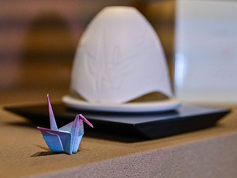 A paper crane next to small dome-shaped lamp (R) - partly glazed from the ashes of burnt paper cranes.