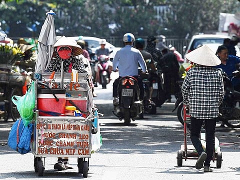 Street vendor Vu Thi Phuong (L) pushes her trolley to sell coffee and soft drinks in Hanoi on June 1, 2023. The north of Vietnam has been struck by heatwaves in recent weeks. 