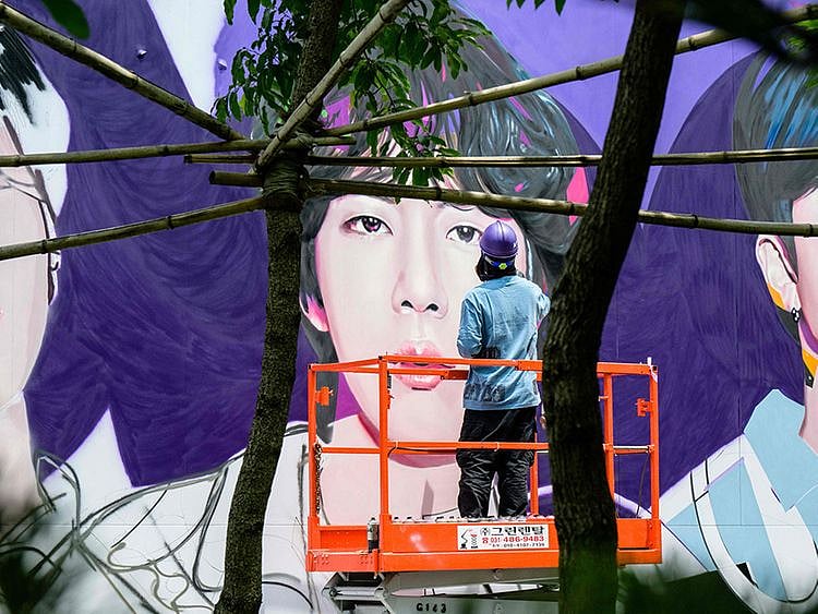 An artist spray paints a mural of K-pop megastars BTS in Seoul on June 12, 2023, on the occasion of the supergroup's 10-year anniversary. Fans of K-pop megastars BTS flocked to hotspots around Seoul on June 12 to mark the supergroup's 10-year anniversary, with South Korea unveiling a special commemorative stamp series to celebrate.