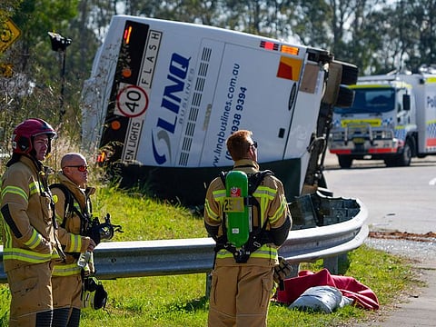 Emergency crews stand near a bus that rolled onto its side near Greta in the Hunter Valley, north of Sydney, Australia, Monday, June 12, 2023. 