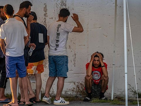Survivors of a shipwreck stand outside a warehouse at the port in Kalamata town, on June 14, 2023, after a boat carrying dozens of migrants sank in international waters in the Ionian Sea. Greece has declared three days of mourning, the interim prime minister's office said on June 14, 2023, over a migrant boat sinking in the Ionian Sea feared to have claimed hundreds of lives.  
