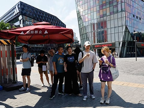 People stand in the shade amid an orange alert for heatwave, at a shopping area in Beijing, China June 22, 2023.  