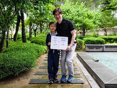 In this picture taken in Seoul on June 21, 2023, Yoon Jae-ha (L), poses with a whiteboard showing his international age, 8, and Korean age, 9, next to his father, Yoon Dong-gun, who works in trade, and whose international age is 43 and Korean age 44. 
