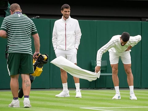 A member of the ground staff uses a leaf blower and Serbia's Novak Djokovic wafts his towel to assist with drying the court as Argentina's Pedro Cachin looks on after a rain break in their first round men's singles match in London on Monday.