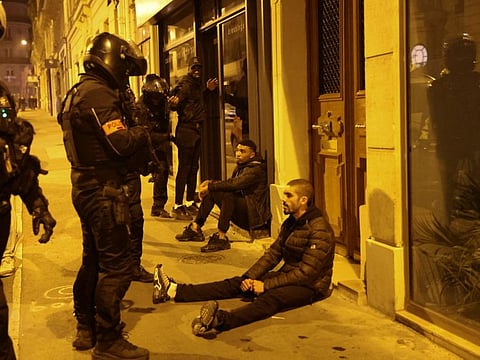 Men sit on a sidewalk as police officers stand next to them during protests following the death of Nahel, a 17-year-old teenager killed by a French police officer in Nanterre during a traffic stop, in Paris, France, July 2, 2023.  