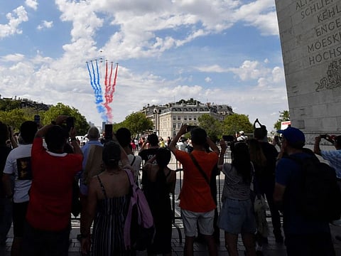 Pedestrians gathered under the Arc de Triomphe take pictures of Alphajets from the French Air Force Patrouille de France releasing trails of red, white and blue smoke, the colours of the French national flag during a rehearsal, three days ahead of the Bastille Day parade on the Champs-Elysees avenue, on July 11, 2023 in Paris.  