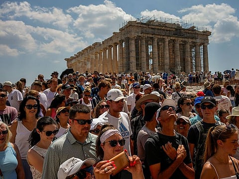 Atop the Acropolis ancient hill, tourists visit the Parthenon temple, background, in Athens, Greece