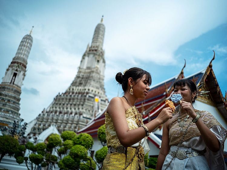 Women dressed in traditional Thai costumes eat ice creams shaped like tiles of the famous Wat Arun temple, or Temple of Dawn, in Bangkok. 