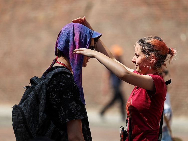 A woman puts wet head scarf to protect a man from the sun, during a heatwave across Italy as temperatures are expected to rise further in the coming days, in Bologna, on July 18, 2023.