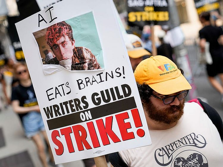 A signed disparaging artificial intelligence technology is carrier while striking writers and actors walk a picket line, Monday, July 17, 2023, in New York. Three years after the pandemic brought Hollywood to a standstill, the film and TV industry has again ground to a halt. This time, though, the industry is engaged in a bitter battle over the how streaming — after advancing rapidly during the pandemic — has upended the economics of entertainment.