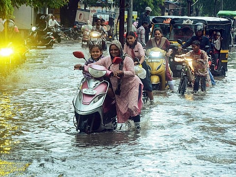 Commuters wade through the waterlogged road after a heavy rainfall, in Nagpur.