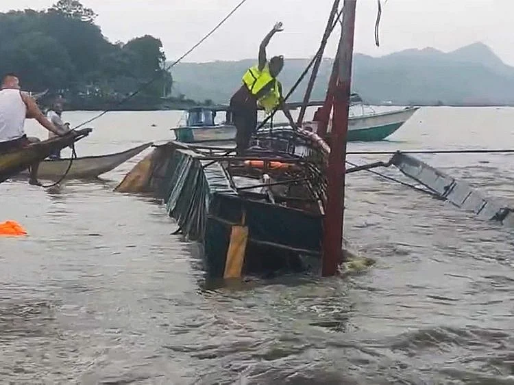 In this image from video provided by the Philippine Coast Guard, a man stands on a capsized passenger boat as they undergo rescue operations at Binangonan, Rizal province, east of Manila, Philippines on Thursday July 27, 2023.  