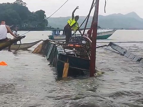 In this image from video provided by the Philippine Coast Guard, a man stands on a capsized passenger boat as they undergo rescue operations at Binangonan, Rizal province, east of Manila, Philippines on Thursday July 27, 2023.  