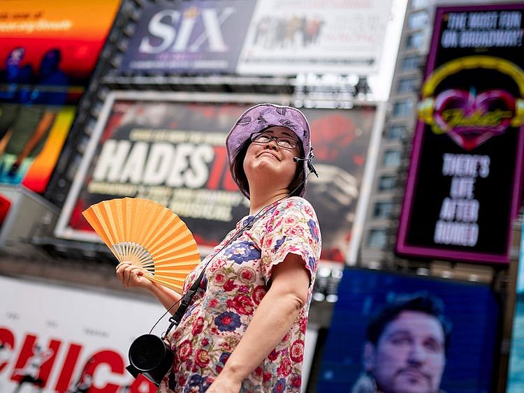 A tour guide fans herself while working in Times Square as temperatures rise, in New York