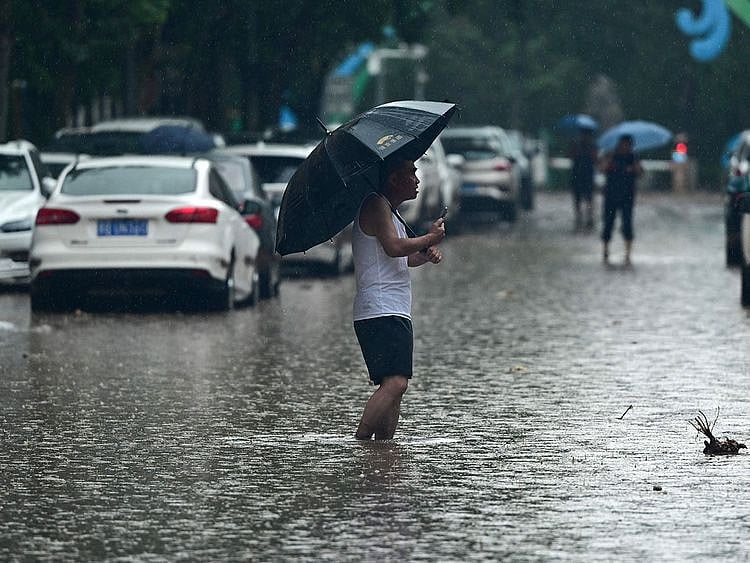 People wade along a flooded street, amid heavy rains in Mentougou district in Beijing on July 31, 2023. Heavy rains battered northern China on July 31, killing at least two people in Beijing while washing away cars and inundating subway stations, with the capital issuing its highest alerts for flooding and landslides.