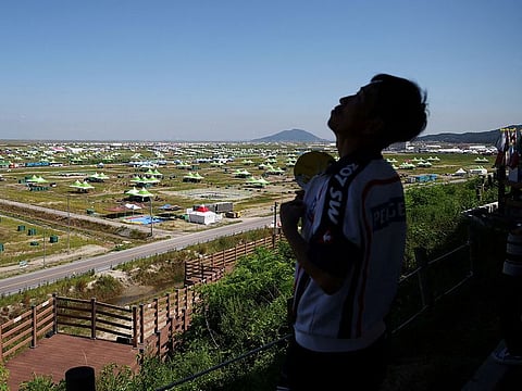 A man fans himself to cool down as an empty camping site of the 25th World Scout Jamboree is seen in the background in Buan, South Korea.