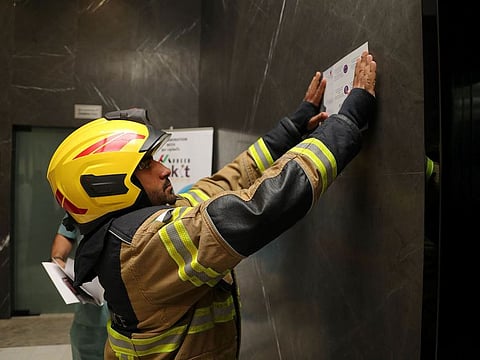 Sharjah Civil Defence placing a safety awareness poster in the lobby of a residential tower, as part of the field visits