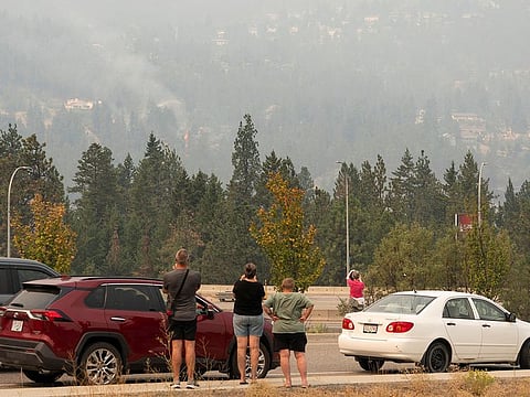 People park at a viewpoint along Bayview Ct to check on their homes as flames erupt during the McDougall Creek wildfire in West Kelowna, British Columbia, on August 19, 2023. 