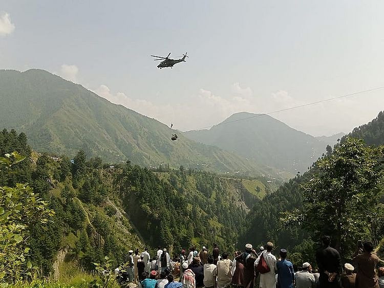 People watch as an army soldier slings down from a helicopter during a rescue mission to recover students stuck in a chairlift in Pashto village of mountainous Khyber Pakhtunkhwa province, on August 22, 2023.  