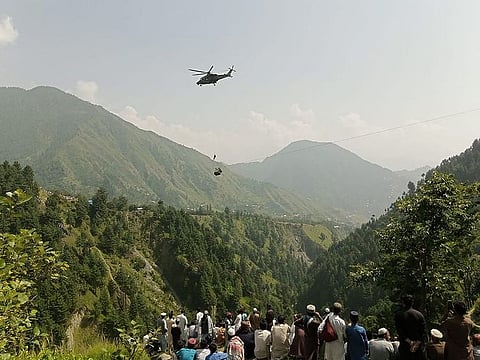 People watch as an army soldier slings down from a helicopter during a rescue mission to recover students stuck in a chairlift in Pashto village of mountainous Khyber Pakhtunkhwa province, on August 22, 2023.  