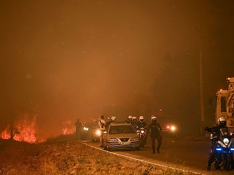 Policemen stand on a road during a wildfire in Chasia in the outskirts of Athens.