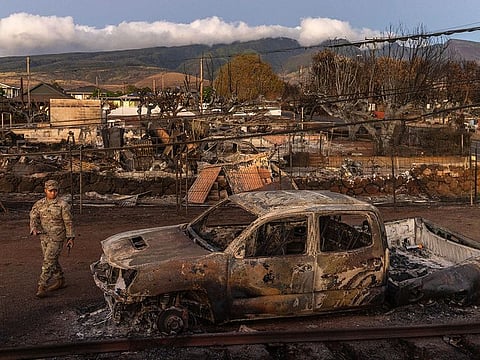 A member of the National Guard walks around a burned pickup in the wildfire-ravaged town of Lahaina, Hawaii.