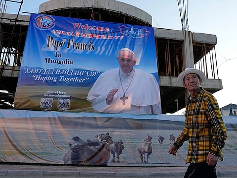 A Mongolian man walks past a banner promoting the visit of Pope Francis near a church in Ulaanbaatar, Mongolia on Monday, Aug. 28, 2023.  