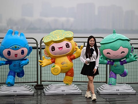 A woman poses for photographs with the 2022 Asian Games mascots along the promenade of Qiantang river in Hangzhou.