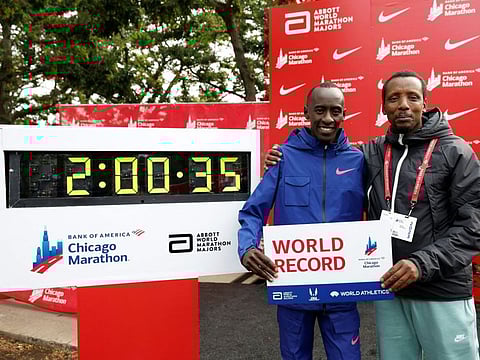 Kenya's Kelvin Kiptum poses with his coach Rwandan Gervais Hakizimana (right) next to the clock marking Kiptum's time after winning the Chicago Marathon in a world record time on Sunday.
