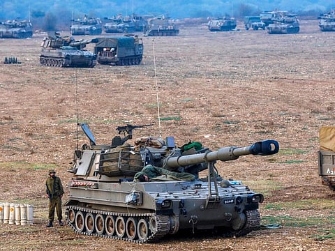An Israeli soldier rests on an artillery cannon as his comrade stands guard at an undisclosed location in northern Israel bordering Lebanon on October 8, 2023.  