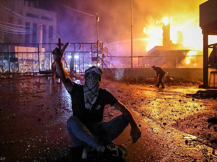 A Lebanese protester flashes the V for victory sign on October 18 as a fire rages behind the security gate of the US embassy after clashes with security forces during a demonstration in solidarity with the people of Gaza in Awkar, East of Beirut, following a blast ripped through a hospital in the Gaza Strip, killing at least 500 people on October 17, 2023.  