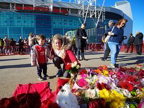 People lay tributes and flowers at the base of the 'United Trinity' sculpture, depicting former Manchester United players George Best, Denis Law and Bobby Charlton, following the death of Bobby Charlton, outside of Old Trafford football stadium in Manchester, central England, on Sunday.