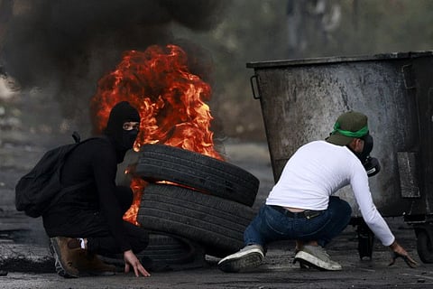 Palestinian youths take cover behind a rubbish container as they clash with Israeli forces at the northern entrance of the West Bank city of Ramallah near the Israeli settlement of Beit El on October 20, 2023, as battles continue between Israel and the Palestinian Hamas group.  