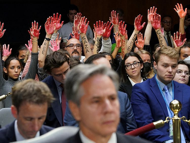 Anti-war protesters raise their "bloody" hands behind US Secretary of State Antony Blinken