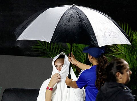 Belarus' Aryna Sabalenka covers from the rain as the match against Kazakhstan's Elena Rybakina is interrupted.