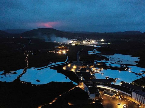 The red shimmer from magma is seen coming out from the erupting Fagradalsfjall volcano behind the tourist land mark Blue Lagoon, near the town of Grindavik  some 40 km west of the Icelandic capital Reykjavik, in this file picture taken on March 20, 2021. 
