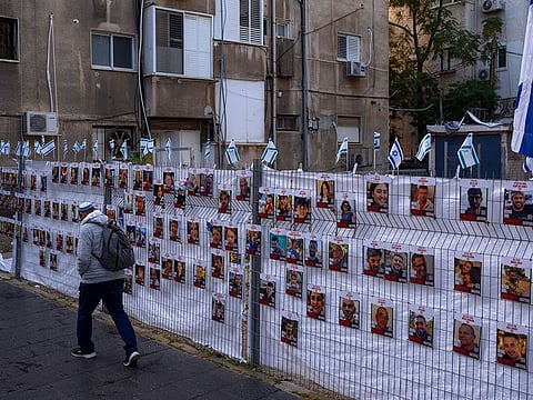 A man passes by a fence with photographs of hostages, mostly Israeli civilians who were abducted during the Oct. 7, unprecedented Hamas attack on Israel, in Ramat Gan, Israel.