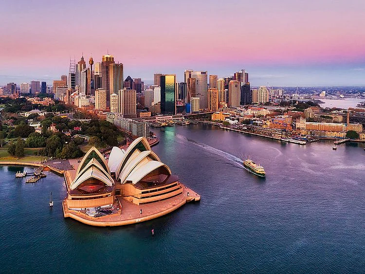Pinkish colourful sunrise over Sydney city CBD on waterfront of Harbour around Circular quay with major architectural landmarks and symbols of Australia.