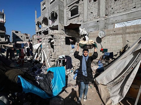 A woman carries bread next to destroyed houses in Rafah on the southern Gaza Strip on December 11, 2023, amid continuing battles between Israel and the militant group Hamas.  